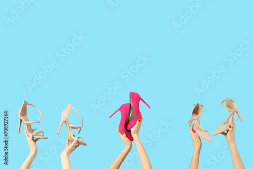 Female hands holding different shoes on blue background © Pixel-Shot