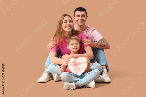 Little boy with gift and his parents sitting on beige background. Valentine's Day celebration