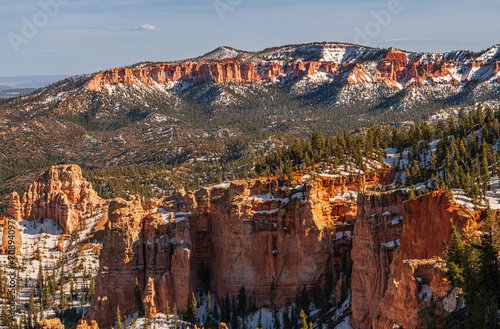 Panorama over Bryce Canyon from a high viewpoint, snow remaining on the ground, clear blue sky, forest, hoodoos.