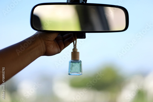 The female driver\'s hand puts the hanging car perfume on the rear view mirror of the car.  perfume packaged in bottles and wooden caps