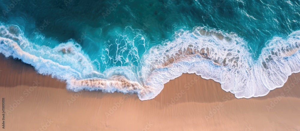 Fototapeta premium Bird's-eye perspective of ocean waves lapping a secluded sandy coast.