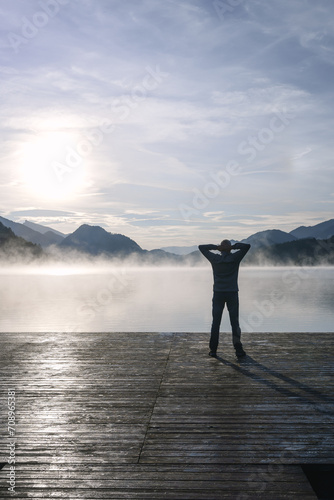 Rückansicht von einem Mann auf einem Holzsteg an einem See. Nebel, Herbst.