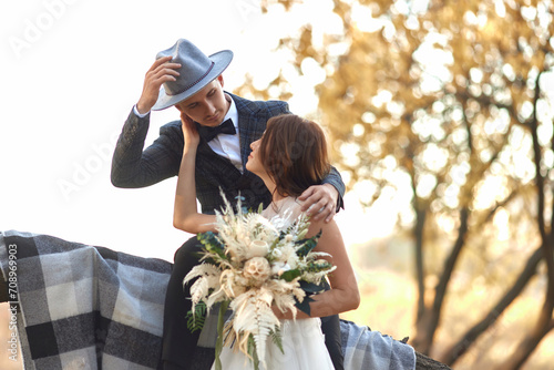 beautiful happy stylish bride and groom in hat near tree in autumn photo