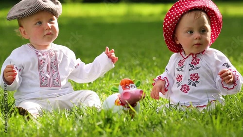 Two cute babies in folk clothes play with toy funny cow on grass photo