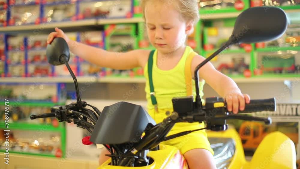 Little boy in yellow sits on toy motorcycle in store with toys Little boy in yellow sits on toy motorcycle in store with toys