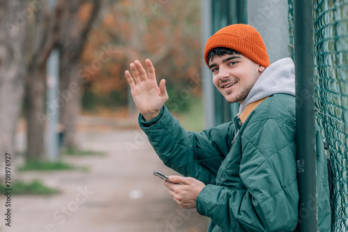 young man in winter on the street waving or calling with his hand with a mobile phone