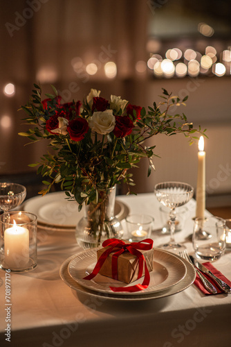 holidays, romantic date and celebration concept - close up of festive table serving for two with gift box, flowers in vase and candles burning at home on valentine's day