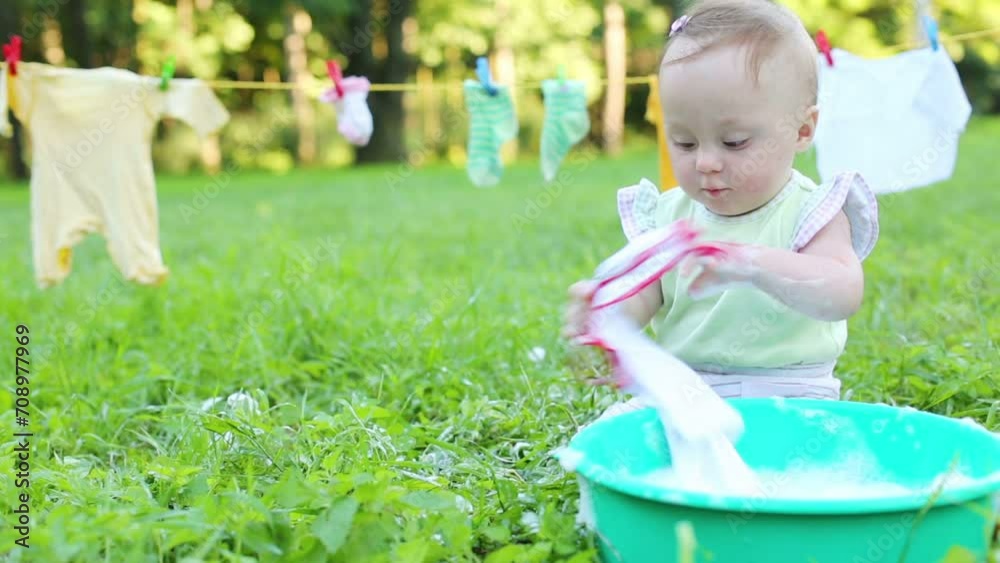 Baby washes clothes in basin on grass at summer. Baby washes clothes in basin on grass at summer.