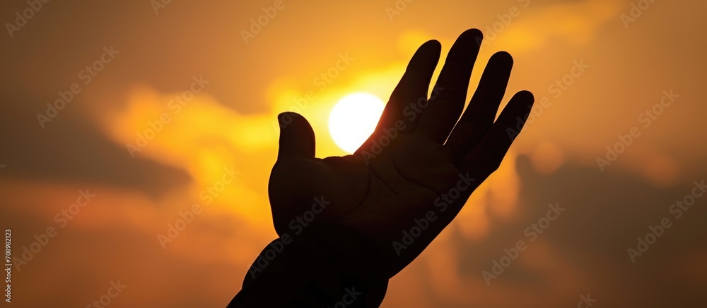 Christian devotee's hand raised in prayer towards Jesus' silhouette.