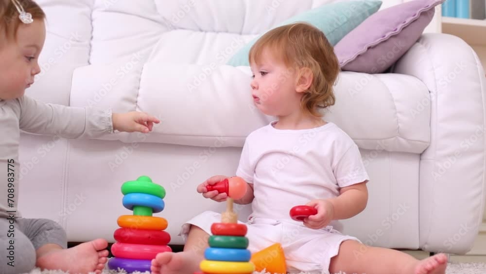 Two barefoot girls sit on carpet and play with pyramids near sofa Two barefoot girls sit on carpet and play with pyramids near sofa