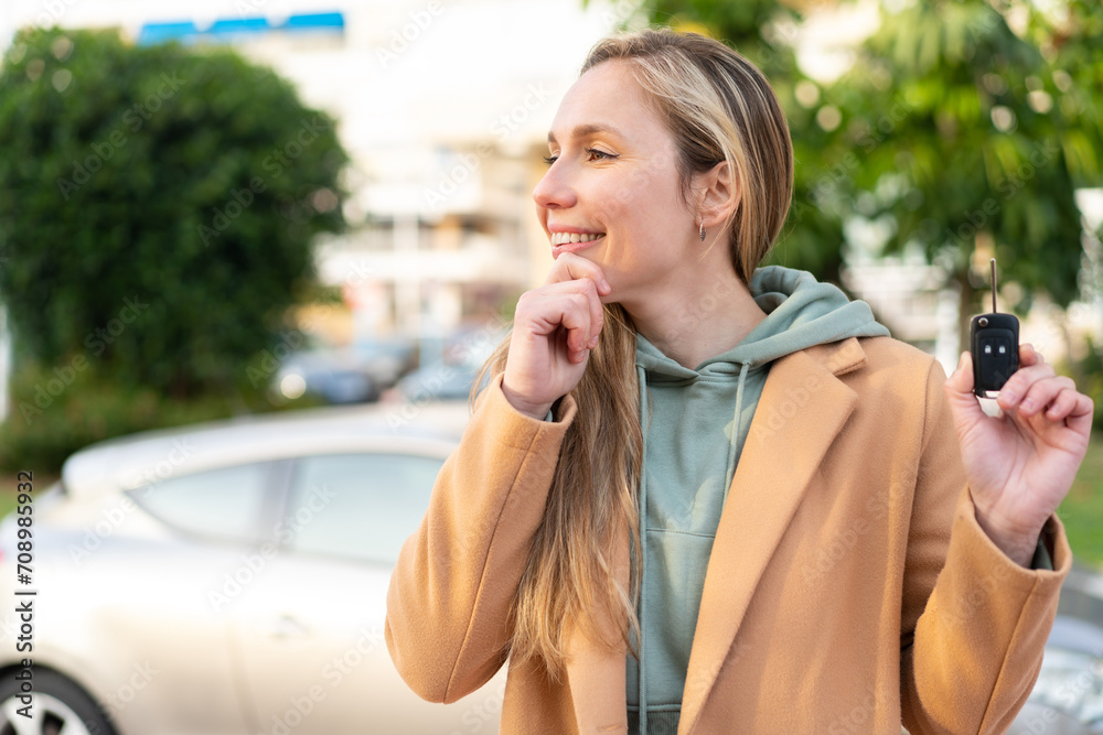 Young blonde woman holding car keys at outdoors thinking an idea and looking side