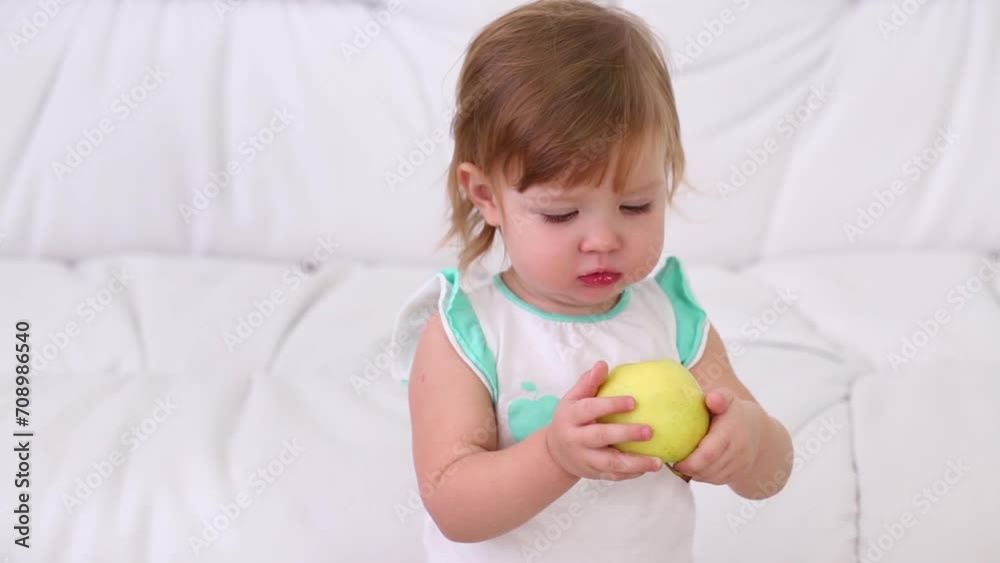 Cute little girl sits on white couch and eats apple at home Cute little girl sits on white couch and eats apple at home