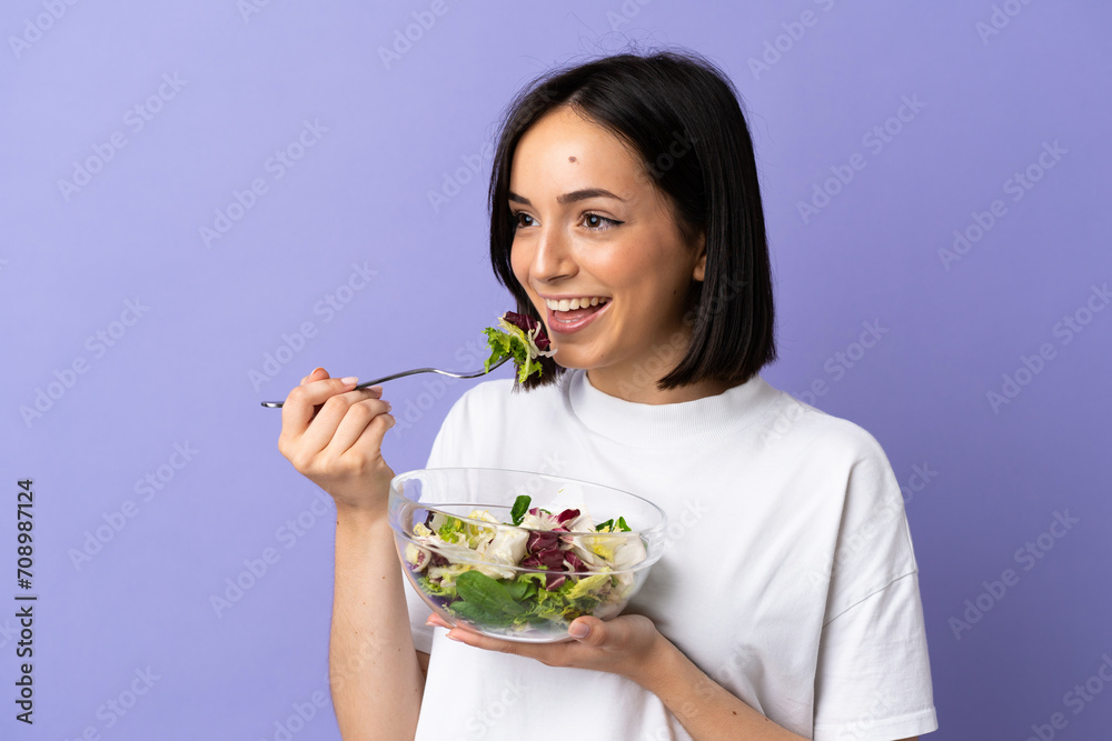 Young caucasian woman isolated on purple background holding a bowl of salad with happy expression Young caucasian woman isolated on purple background holding a bowl of salad with happy expression