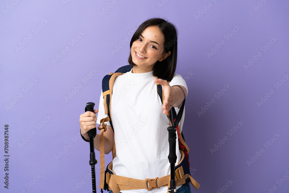 Young caucasian woman with backpack and trekking poles isolated on blue background shaking hands for closing a good deal Young caucasian woman with backpack and trekking poles isolated on blue background shaking hands for closing a good deal