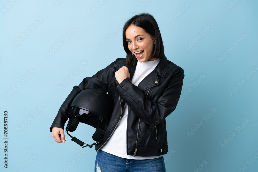 Woman holding a motorcycle helmet isolated on blue background celebrating a victory Woman holding a motorcycle helmet isolated on blue background celebrating a victory