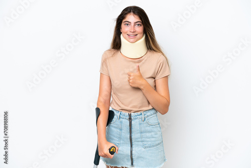 Young caucasian woman wearing neck brace and crutch isolated on white background giving a thumbs up gesture