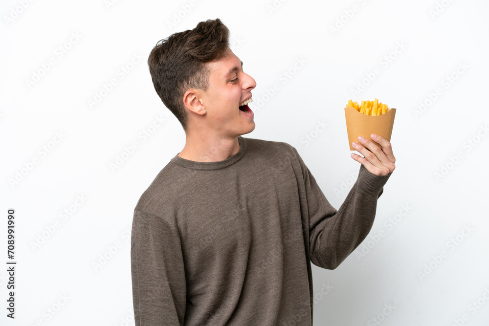 Young Brazilian man holding fried chips isolated on white background laughing in lateral position Young Brazilian man holding fried chips isolated on white background laughing in lateral position