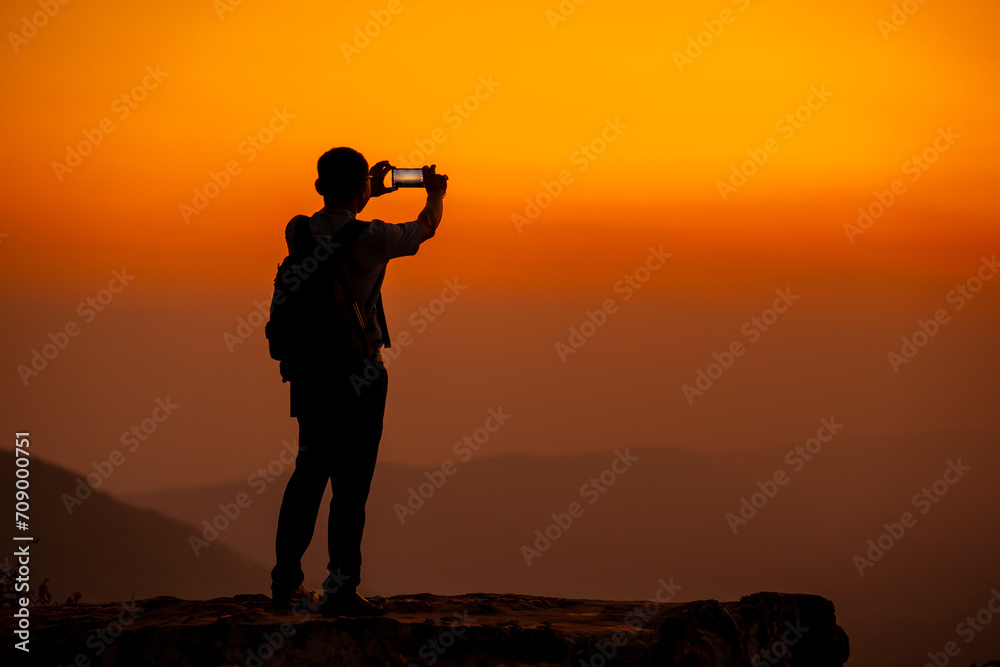 Man hold smartphone on the cliff of the mountain on sunset background