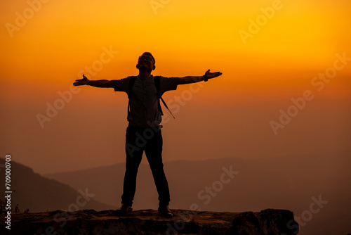 Man tourist on the cliff of the mountain on sunset background