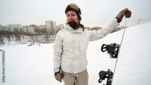 Smiling girl snowboarder stands on a hillside and looks around photo