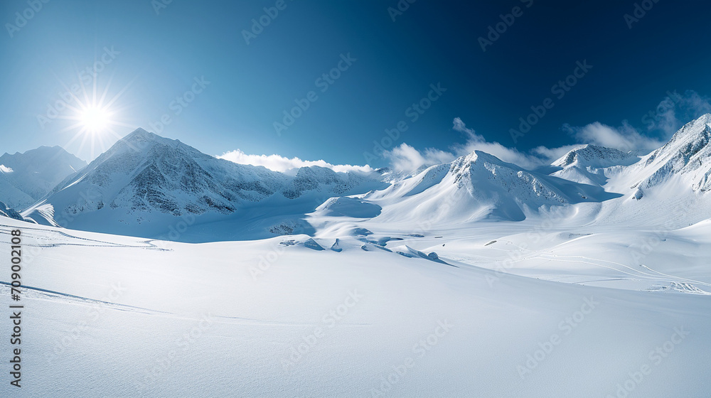 Obraz premium Stunning panoramic view of snowy mountain range. The untouched powder snow with ski tracks crisscrossing. Bright and crisp winter day with snow capped peaks and clear blue sky. Cold adventure and expe