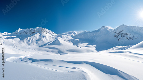 Stunning panoramic view of snowy mountain range. The untouched powder snow with ski tracks crisscrossing. Bright and crisp winter day with snow capped peaks and clear blue sky. Cold adventure and expe