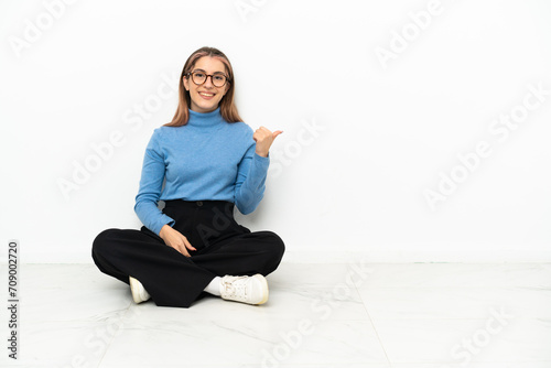 Young Caucasian woman sitting on the floor pointing to the side to present a product