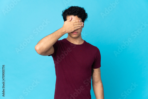 Young Venezuelan man isolated on blue background covering eyes by hands. Do not want to see something