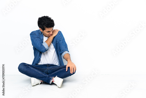 Venezuelan man sitting on the floor suffering from pain in shoulder for having made an effort © luismolinero