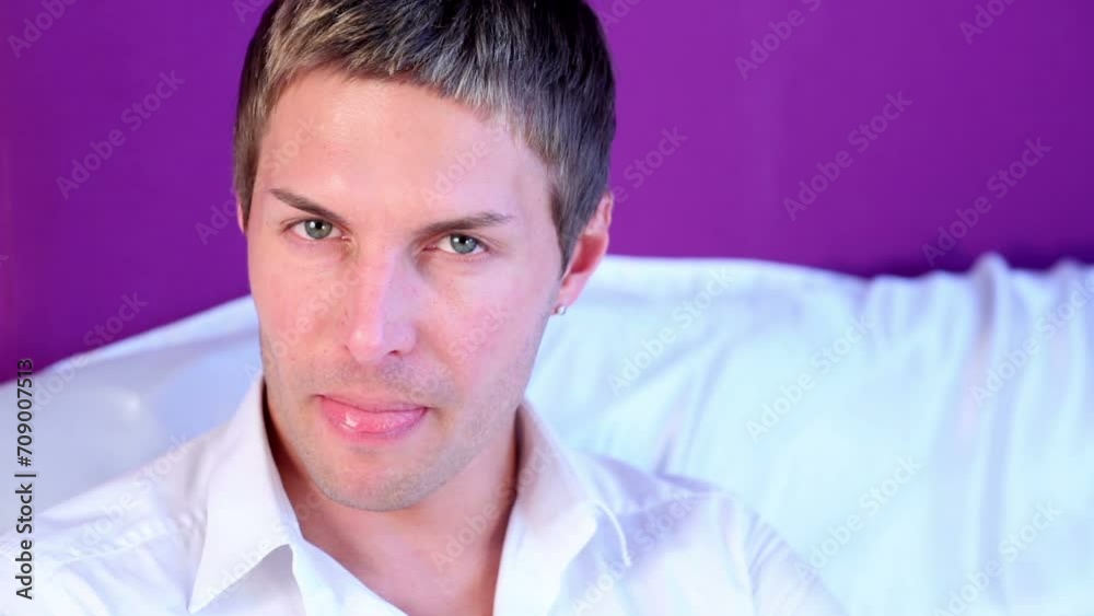 man in shirt with stand-up collar sits on sofa, looking sullenly.