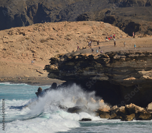 Waves breaking over the cliff with many tourists around, west coast of Fuerteventura, Canary Islands
