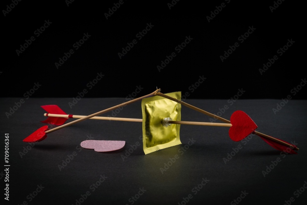 condom pierced by cupid's arrow on a black background condom pierced by cupid's arrow on a black background
