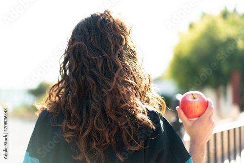 Young sport woman with an apple at outdoors in back position