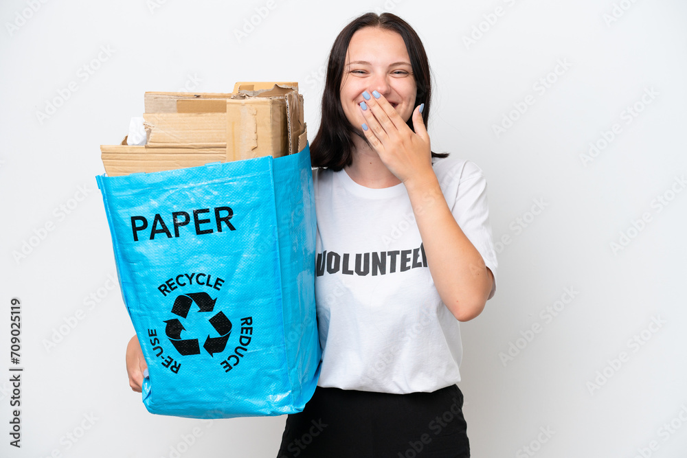 Young caucasian woman holding a recycling bag full of paper to recycle isolated on white background happy and smiling covering mouth with hand Young caucasian woman holding a recycling bag full of paper to recycle isolated on white background happy and smiling covering mouth with hand