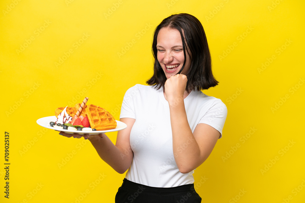Young caucasian woman holding waffles isolated on yellow background celebrating a victory Young caucasian woman holding waffles isolated on yellow background celebrating a victory