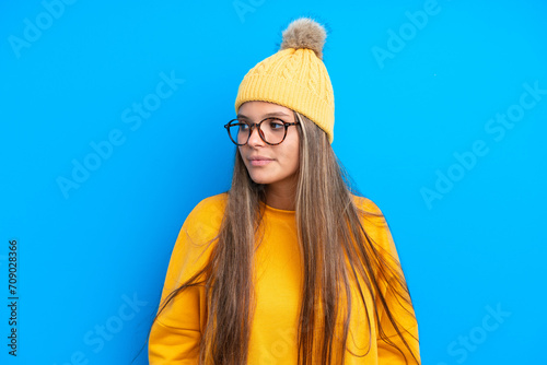 Young caucasian woman wearing winter clothes isolated on blue background looking to the side © luismolinero