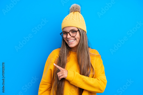 Young caucasian woman wearing winter clothes isolated on blue background pointing to the side to present a product