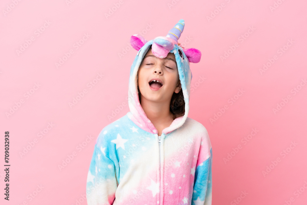 Little caucasian woman wearing a unicorn pajama isolated on pink background laughing