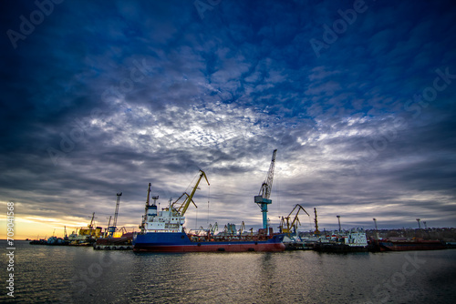 Cargo ship docked at industrial port, cranes ready for unloading. Shipping containers, maritime commerce. Sunset over harbor, global trade, logistics background. Freight transport, import export hub.
