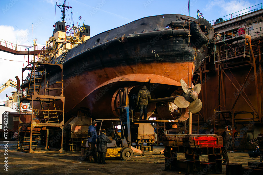 Industrial ship repair and maintenance executed by skilled workers at dry dock. Marine vessel overhaul featuring large propellers, symbolizing naval engineering, trade, and transport infrastructure.