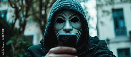 Masked criminal streaming ransom video on dark web  demanding money via smartphone.