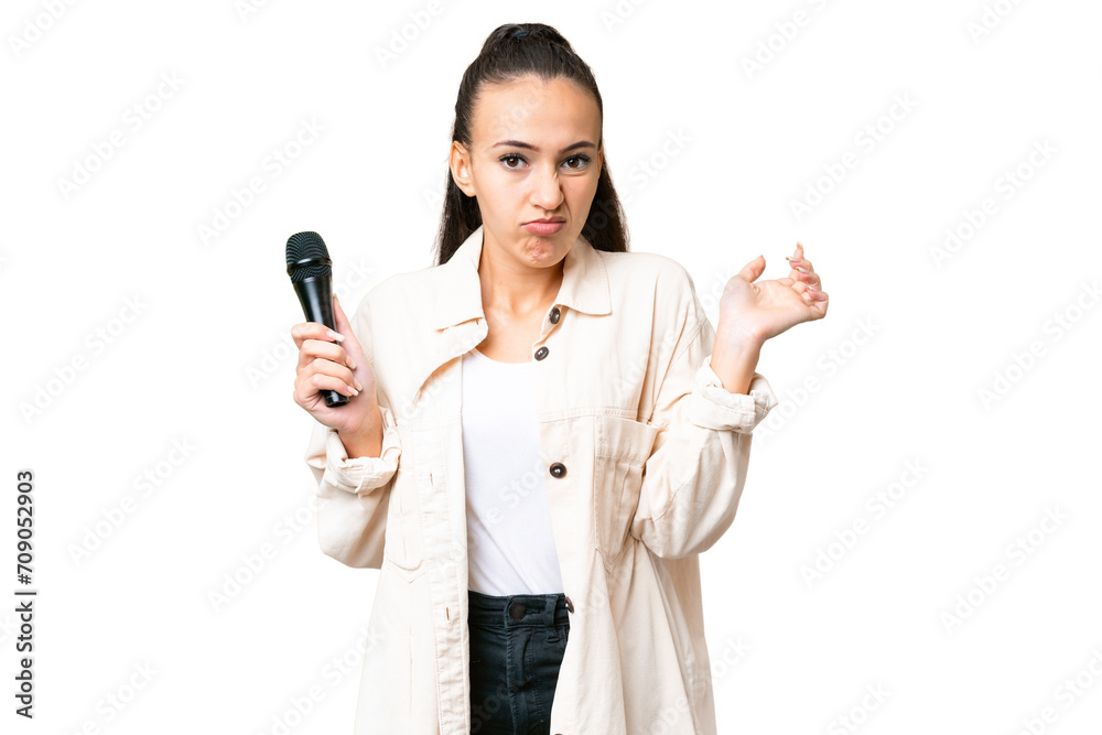Young singer woman picking up a microphone over isolated chroma key background having doubts while raising hands Young singer woman picking up a microphone over isolated chroma key background having doubts while raising hands