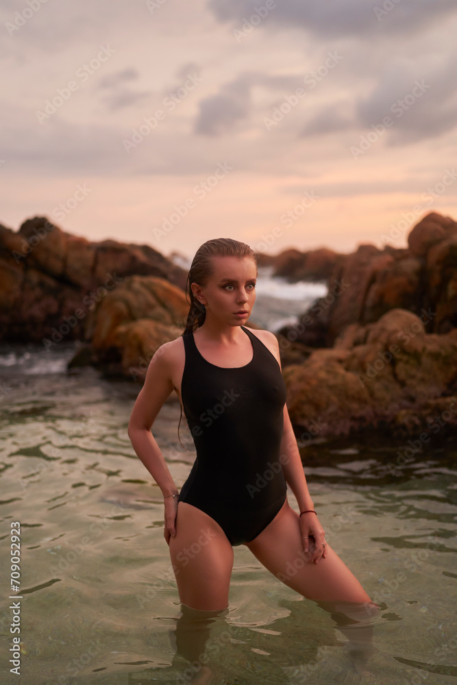 Attractive woman stands in shallow ocean waters at dusk, showcasing wellness and active beach lifestyle. Fit female enjoys serene sea bath, embodies harmony with nature, beauty routine, tranquility.