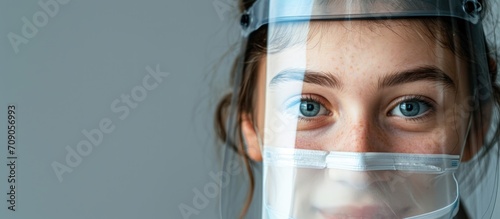 Teen girl with face shield proudly features vaccine band aid, eyes smiling, on gray background, COVID-19. photo