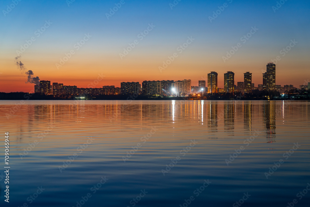 City silhouette on sunset background with lights in the windows of houses