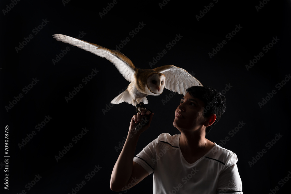 Obraz premium Studio shot of a beautiful baby owl with its wings outstretched and held by a woman. Wild animal.