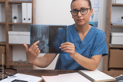 Woman traumatologist points finger at X-ray picture talking to patient online looking at camera doctor consults visitor remotely treatment in modern clinic photo
