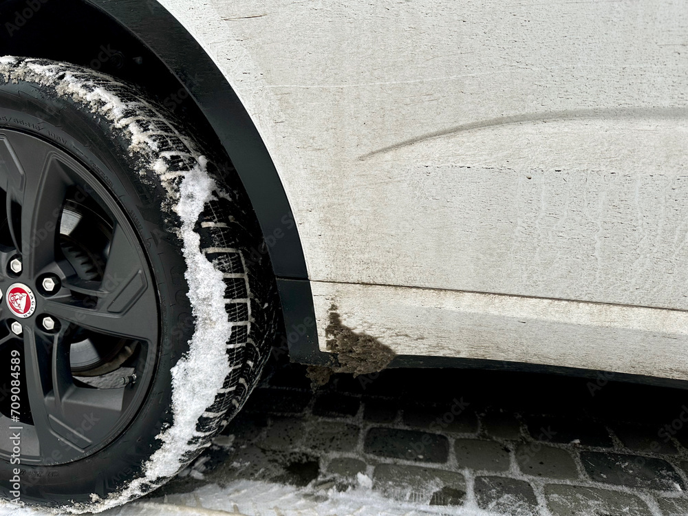 Side view of white Jaguar car with dirty snow stain. Car dirty wheel