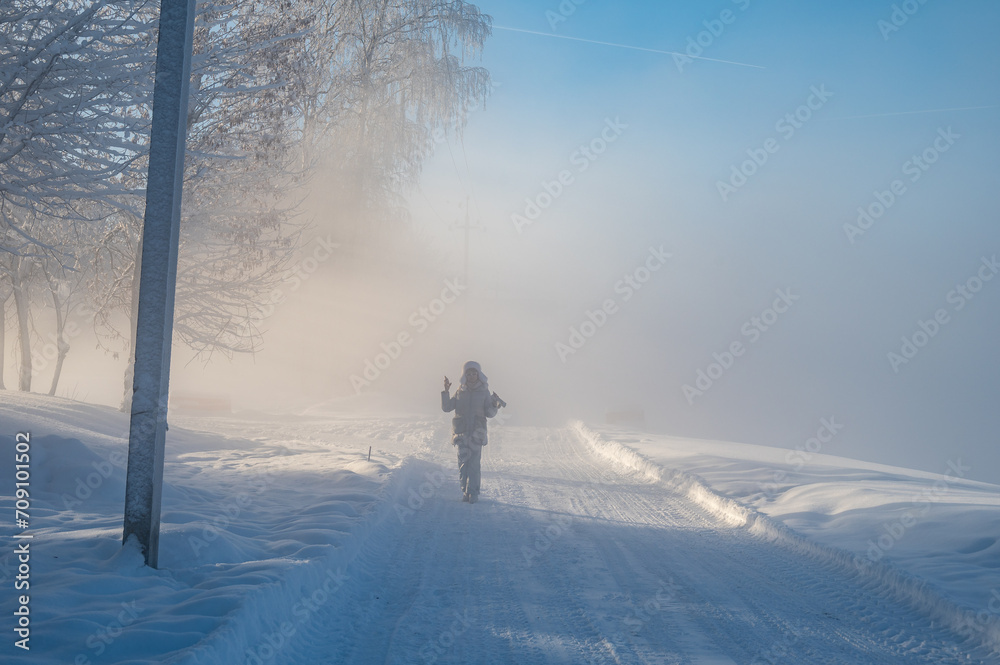 An attractive adult woman in winter clothes stands at full length on the snowy bank of the river. An attractive adult woman in winter clothes stands at full length on the snowy bank of the river.