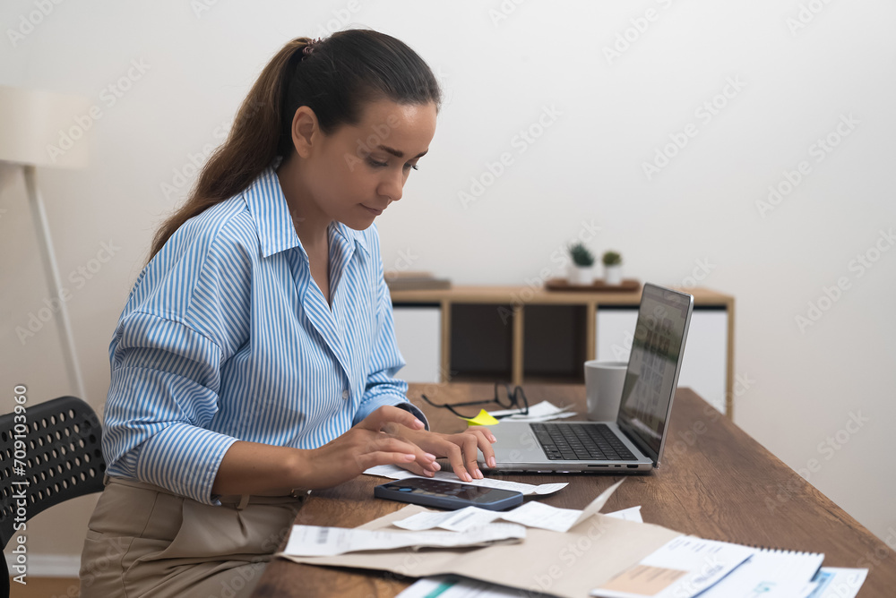 Serious lady calculates utility bills with calculator sitting at desk with laptop woman manages budget keeping track of bank calculations accuracy at home